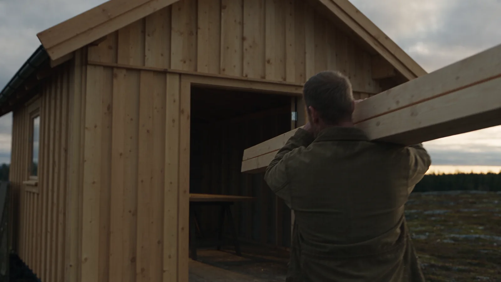 Un charpentier transporte du bois vers une maison en bois en construction. Scène illustrative.
